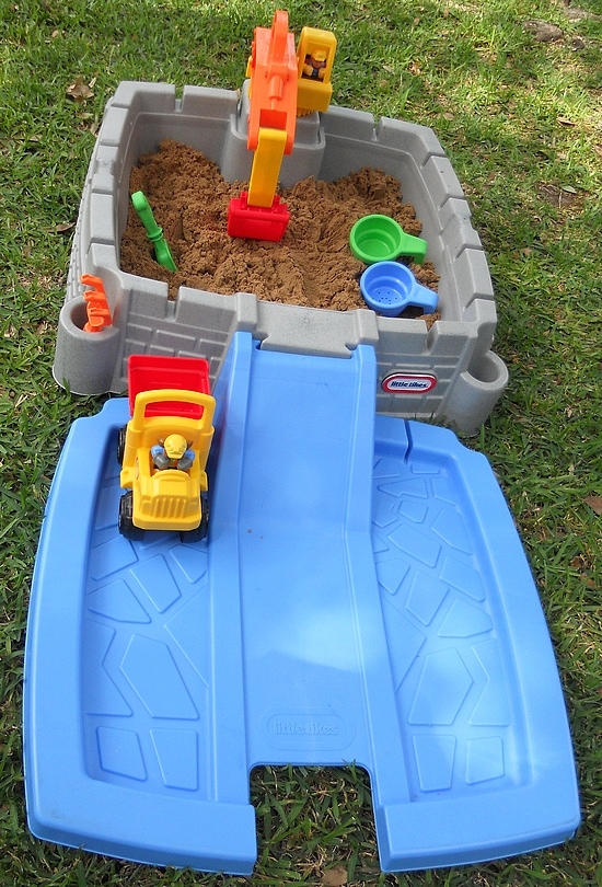 Little Tikes construction sandbox outside in the sun with sand.