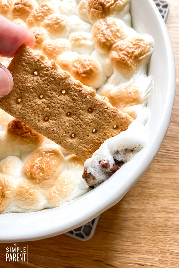 Person dipping graham cracker in oven baked Smores dip