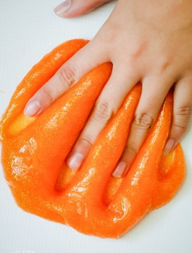Kneading orange glitter glue slime with hands