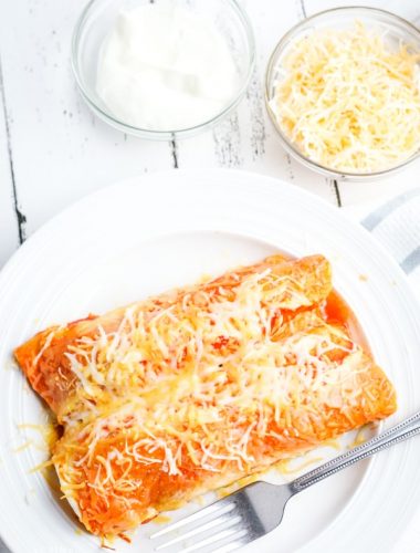 Plate of Crock Pot chicken enchiladas with sour cream and shredded cheese