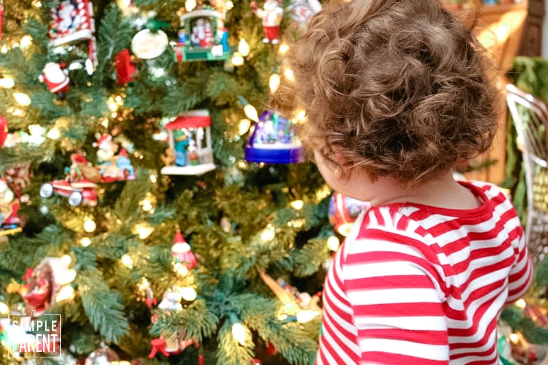 Toddler girl wearing red and white striped shirt while looking at a decorated Christmas tree