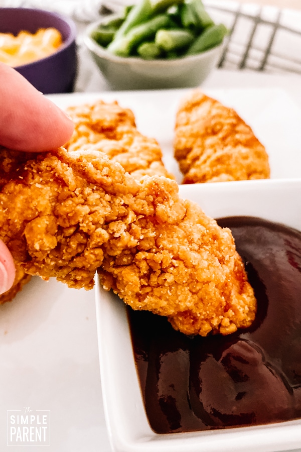 Dipping a crispy chicken strip in barbecue sauce