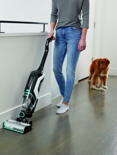 Woman vacuuming floor while dog follows behind her