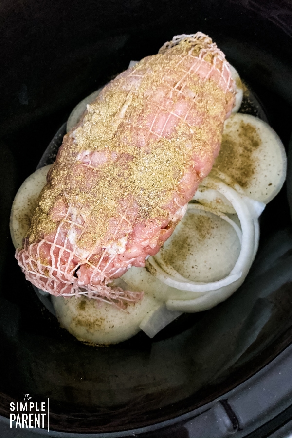 Seasoned turkey breast sitting on top of onions in a slow cooker