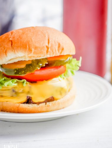 Hamburger with cheese, lettuce, tomato, and pickles on a bun sitting on a white plate