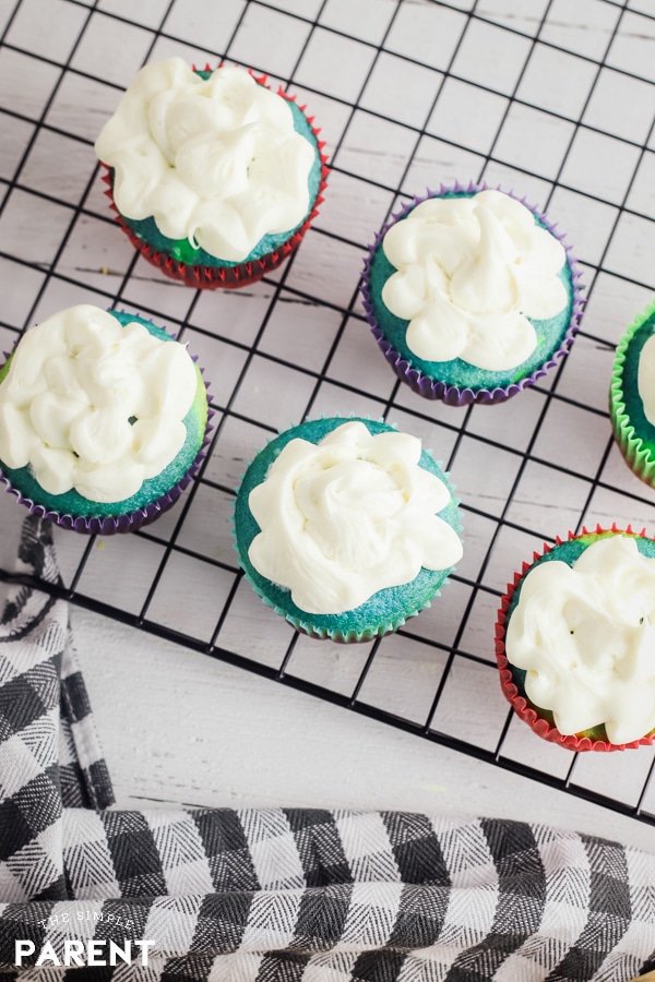 Colorful cupcakes with white frosting sitting on a cooling rack