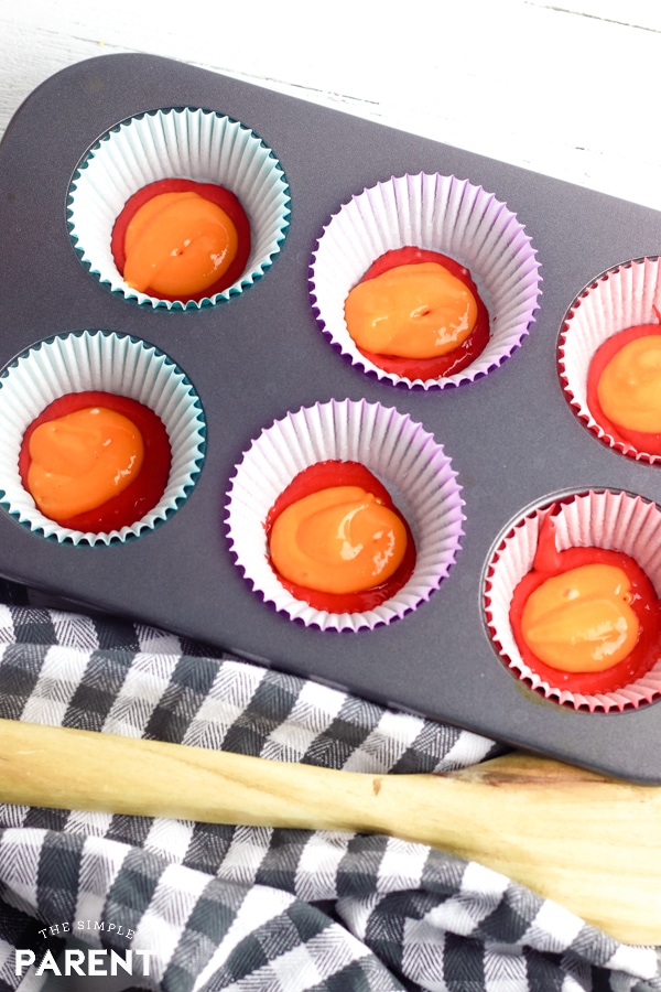 Red and orange cake batter in cupcake liners sitting in a muffin tin