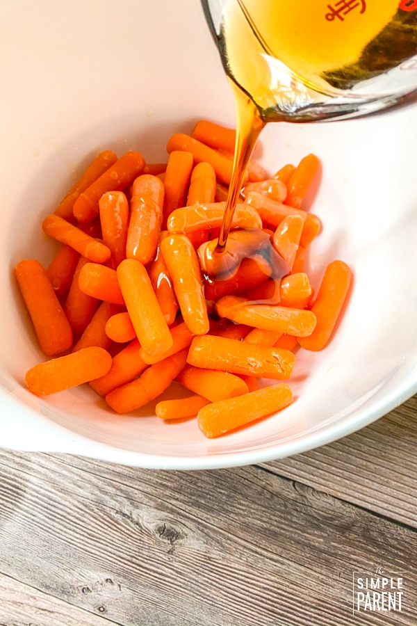 Pouring maple syrup over baby carrots in a bowl