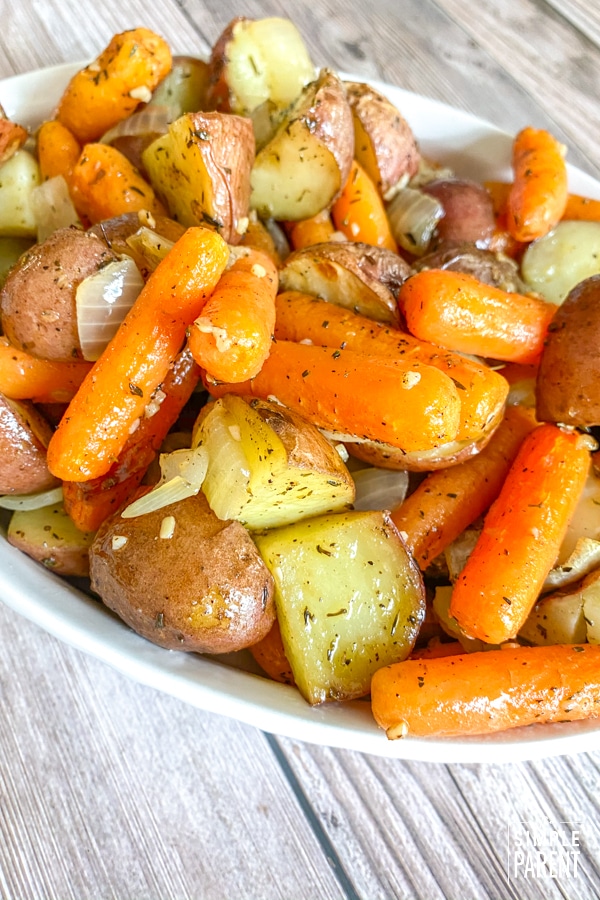 Baby carrots and potatoes with roasted onions in a white serving dish