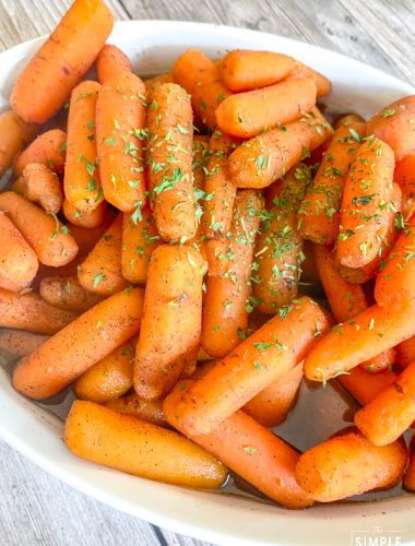 Bowl of glazed baby carrots made in the slow cooker and garnished with parsley flakes