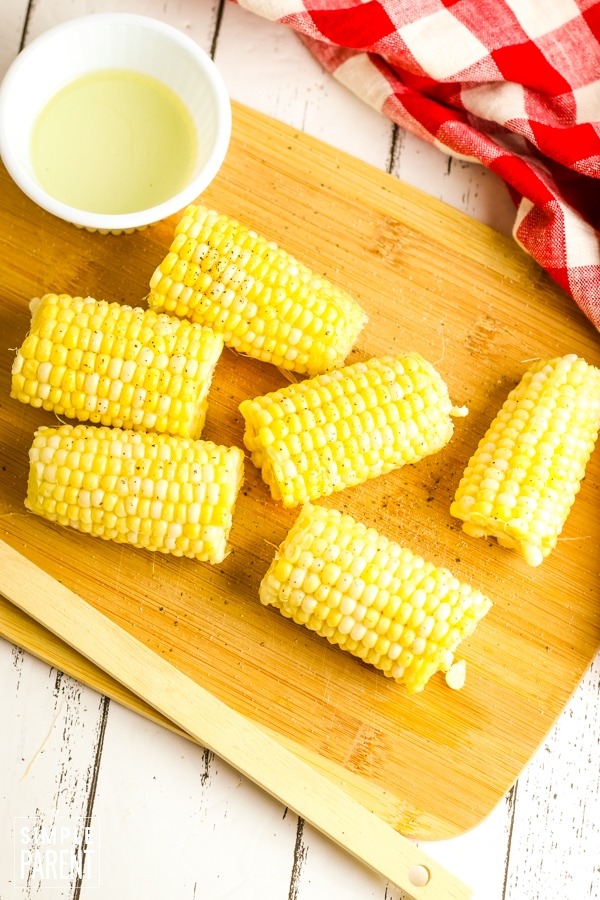 Corn on the cob on cutting board with bowl of olive oil