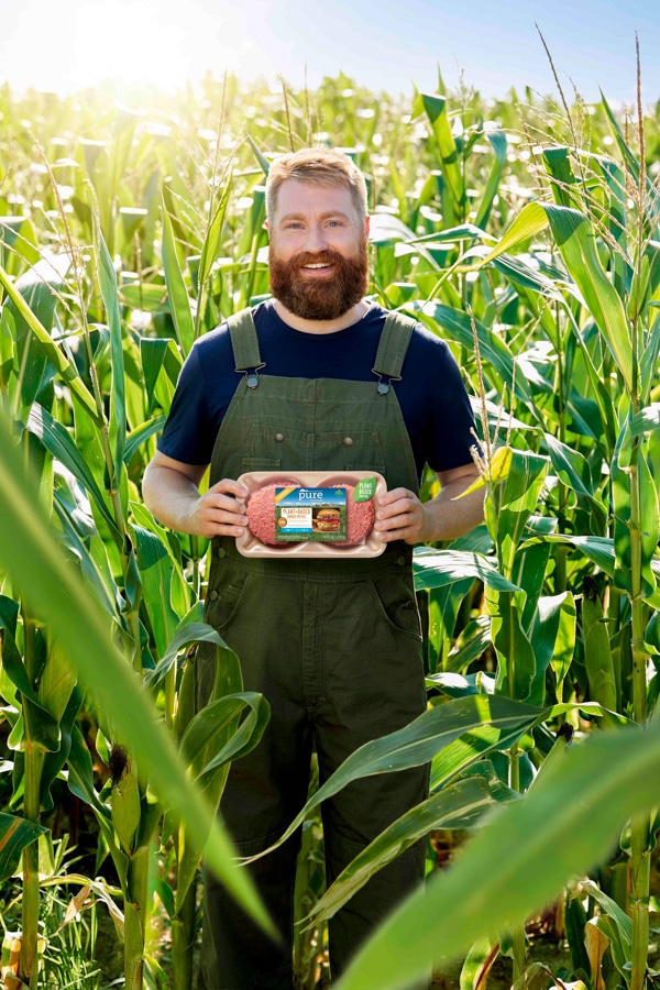 Man holding Pure Farmland burger patties in a corn field