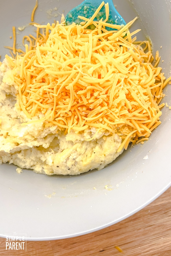 Mashed potatoes and shredded cheese in a mixing bowl