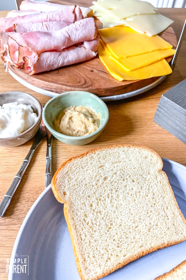 Bread with bowls of condiments and lunch meat and cheese