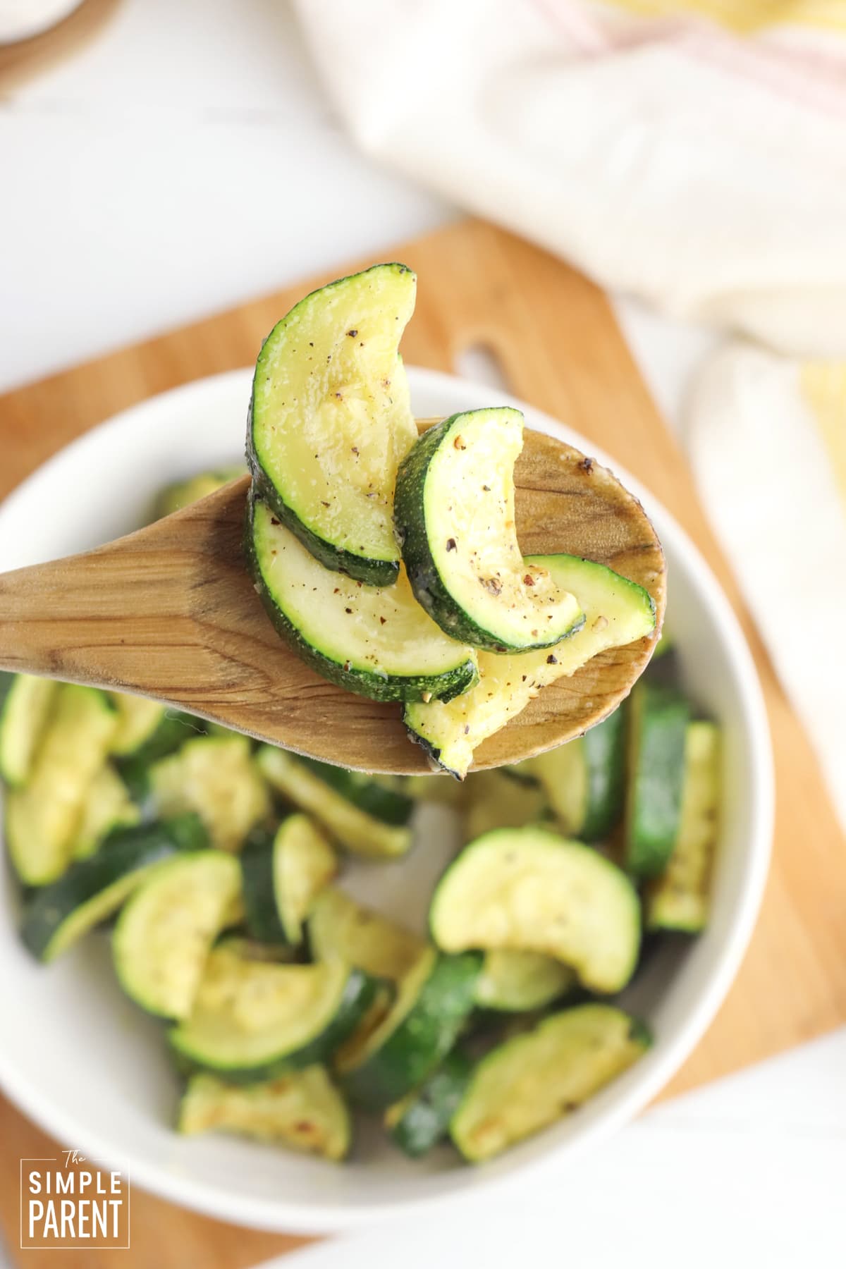 Fried zucchini slices on wooden spoon above white serving bowl