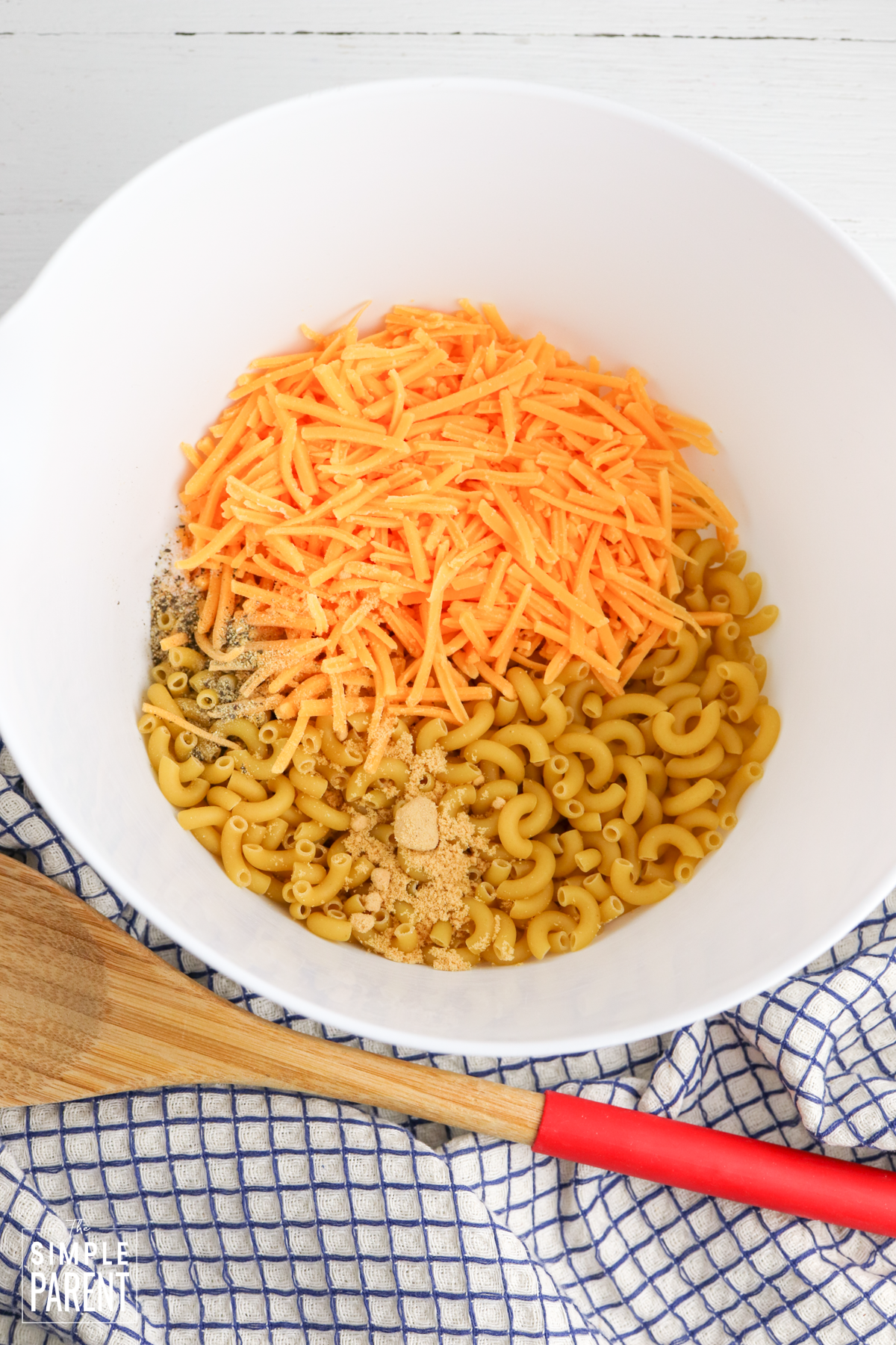 White mixing bowl with air-fried mac and cheese ingredients: elbow mac, shredded cheddar cheese, and seasonings.