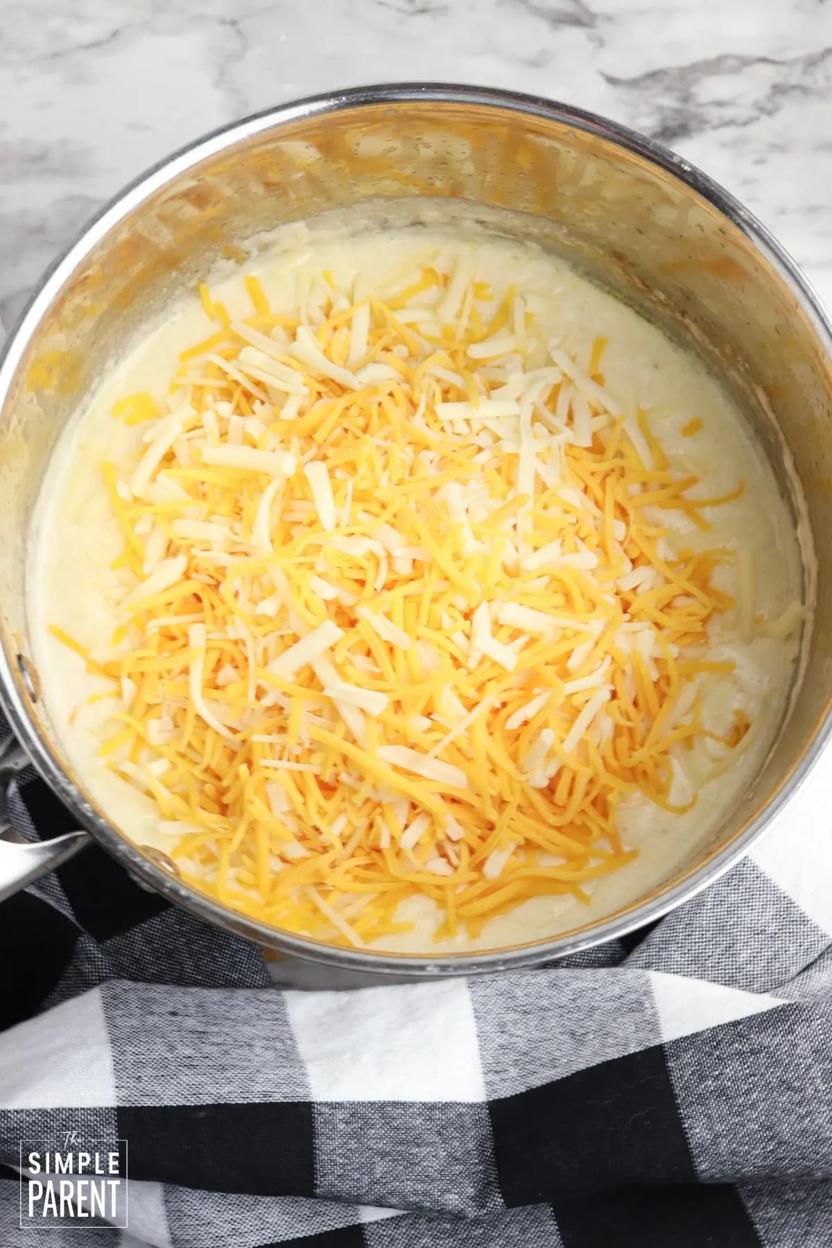 Cooking pan with melted butter and milk topped with shredded cheese.