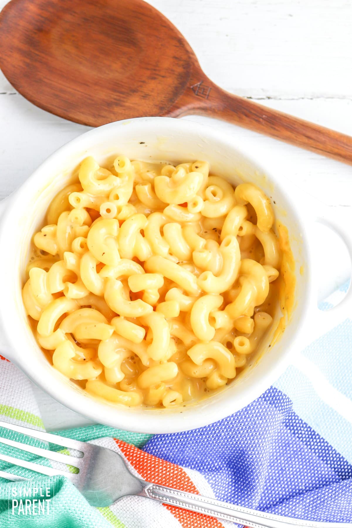 Creamy mac and cheese in white bowl with multicolored napkin and fork