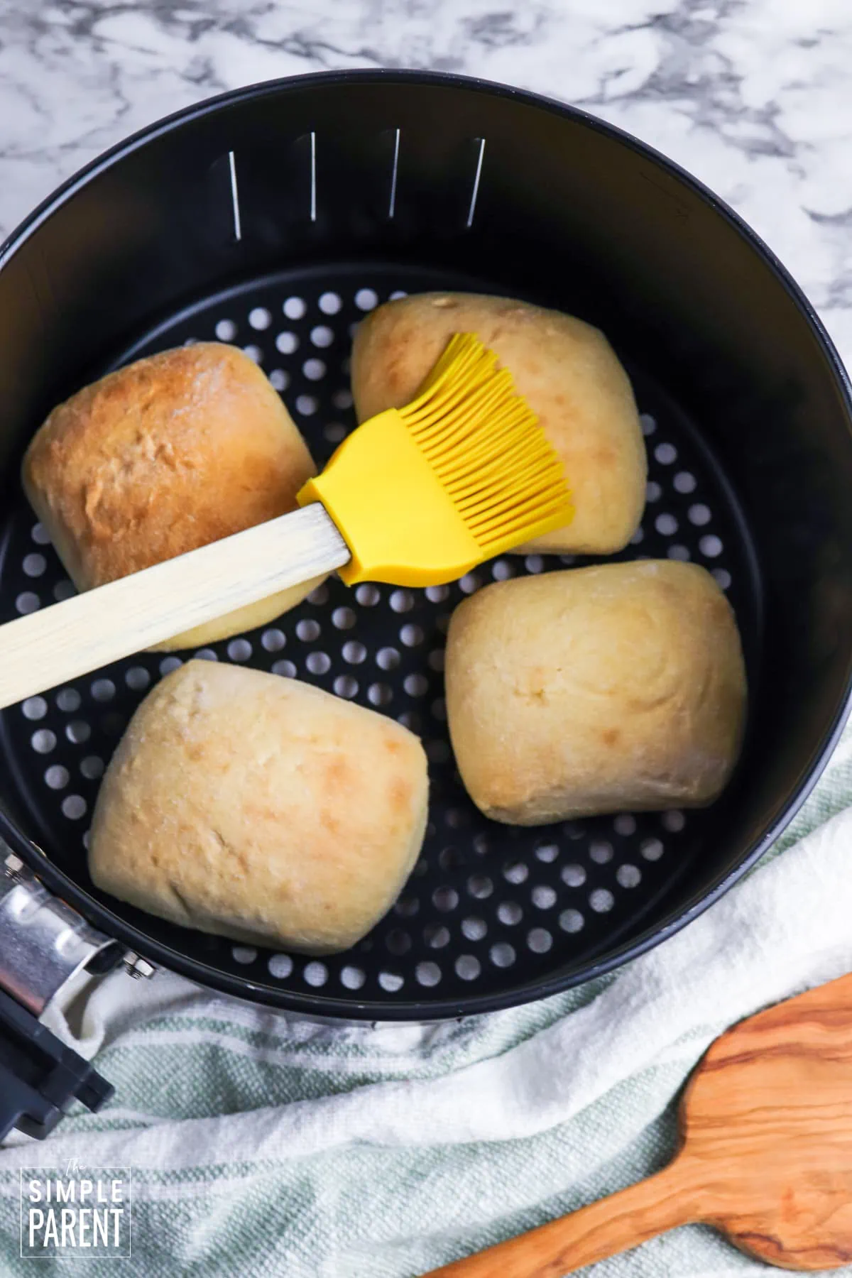 Brushing melted butter on rolls in air fryer basket