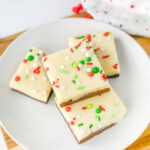 Pieces of layered Christmas Fudge on white plate sitting on wooden cutting board