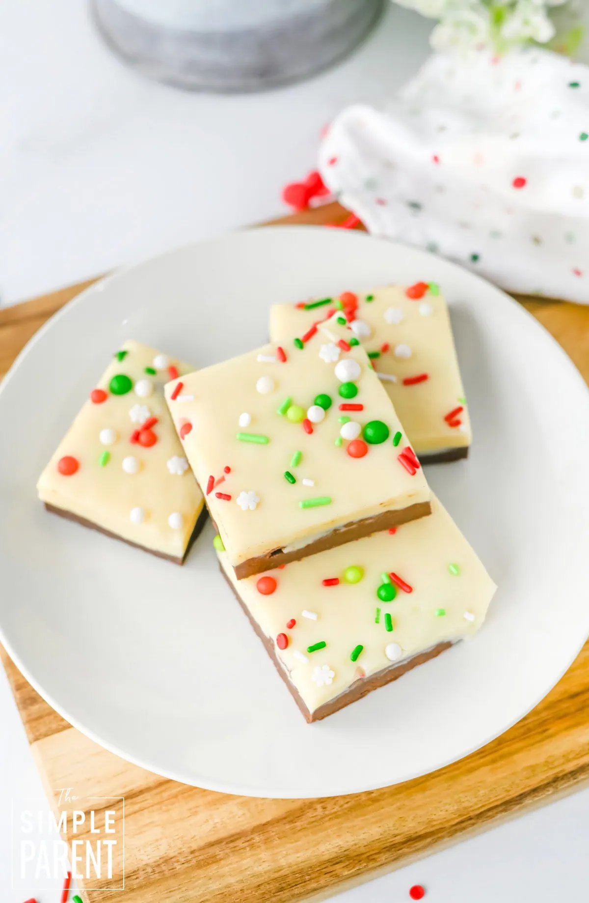 Pieces of layered Christmas Fudge on white plate sitting on wooden cutting board