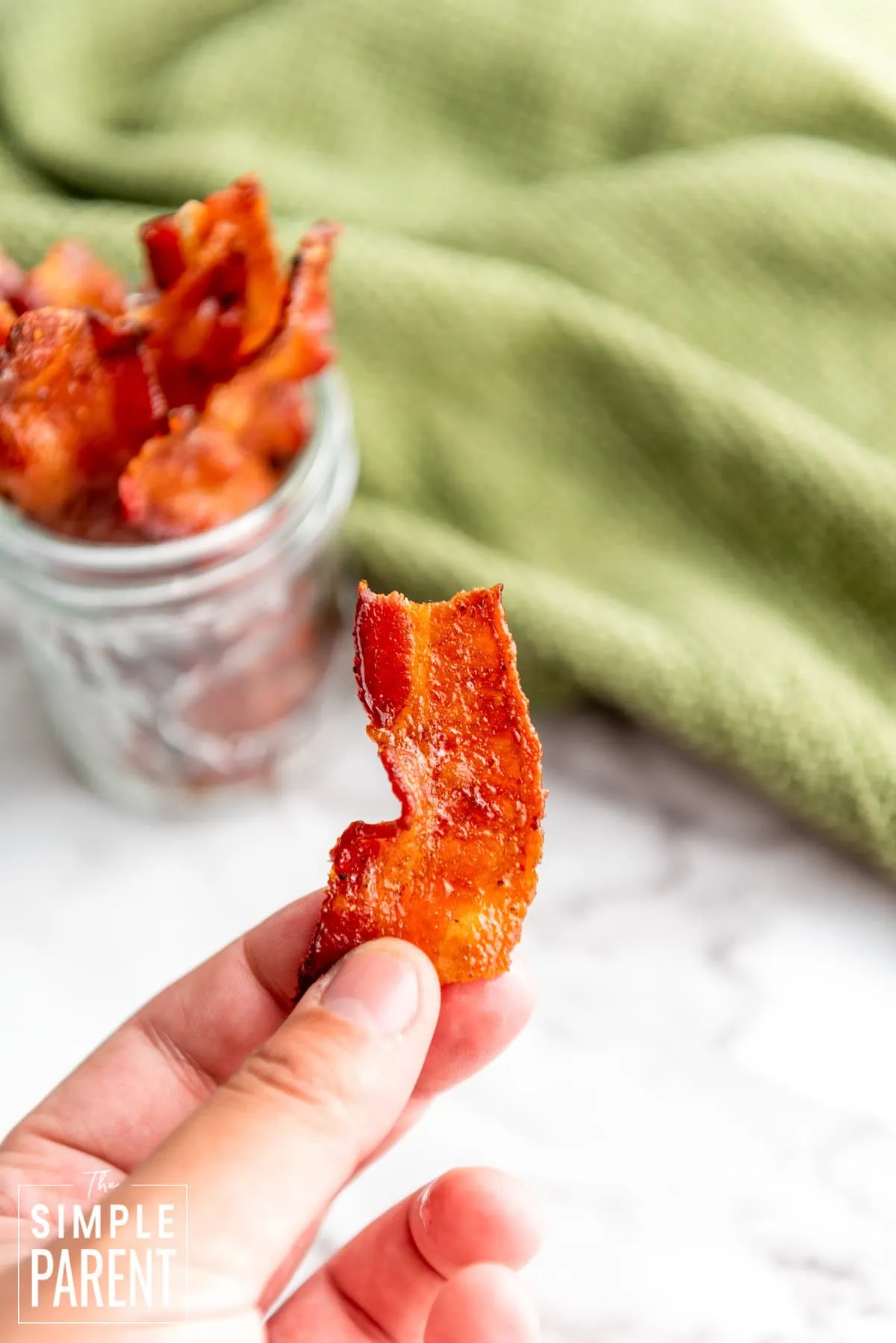 hand holding a piece of caramelized bacon with a jar in the background