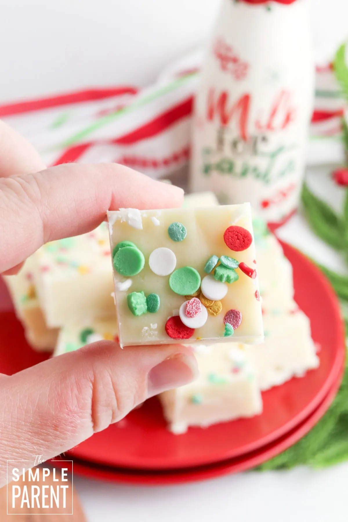 Hand holding a piece of Christmas sugar cookie fudge over a red plate