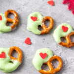 Grinch themed white chocolate covered Christmas pretzels on gray counter