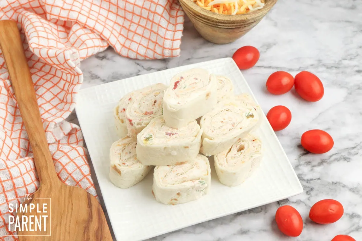 Stack of taco pinwheels on white plate with cherry tomaties