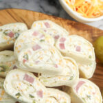 Stack of ham and cheese pinwheels on wooden serving board