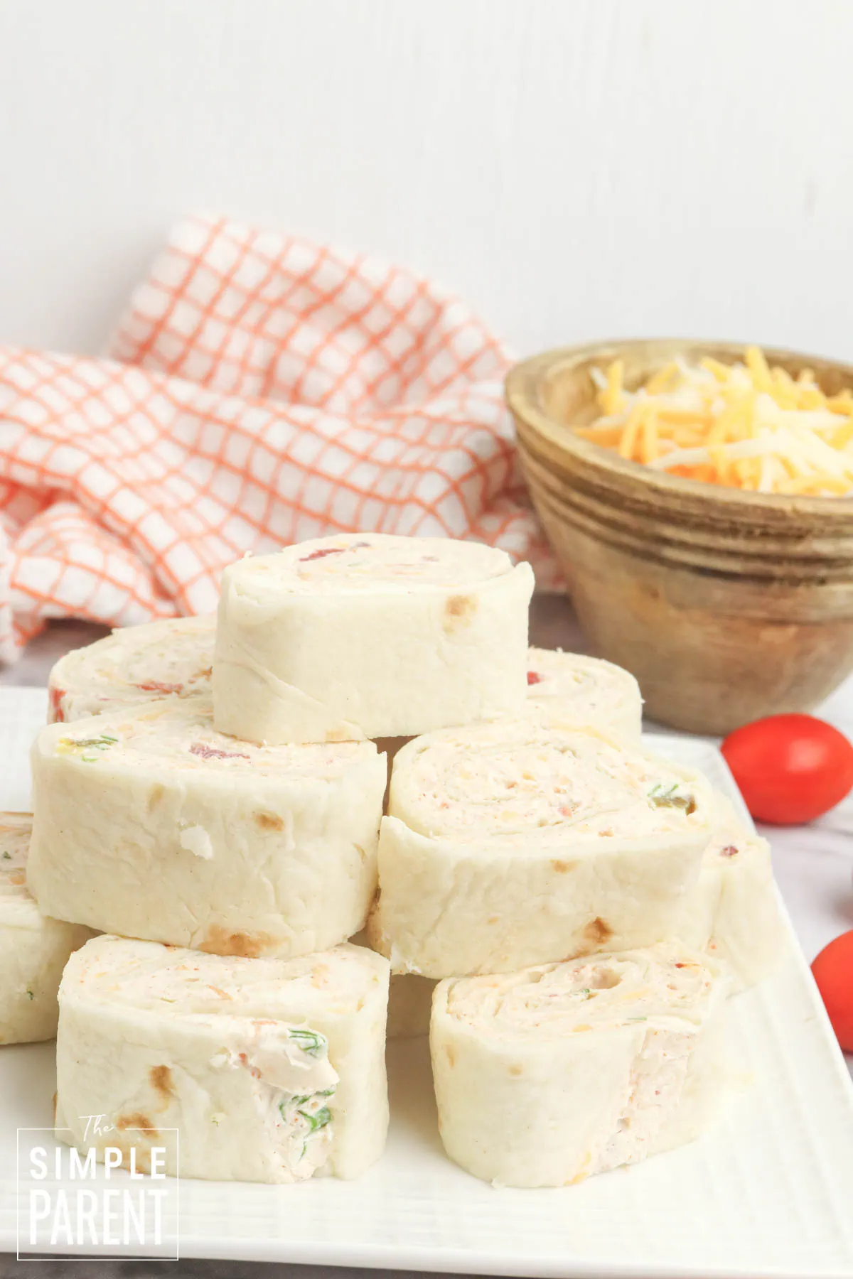 Stack of salsa pinwheels on white plate with brown bowl of cheese