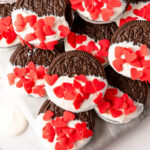 Valentine Oreos dipped in white chocolate with red sprinkles on white counter