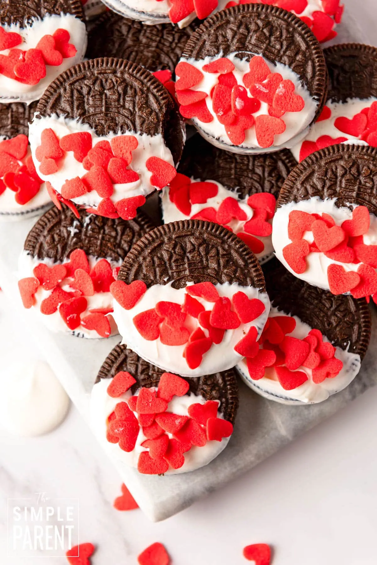 Valentine Oreos dipped in white chocolate with red sprinkles on white counter