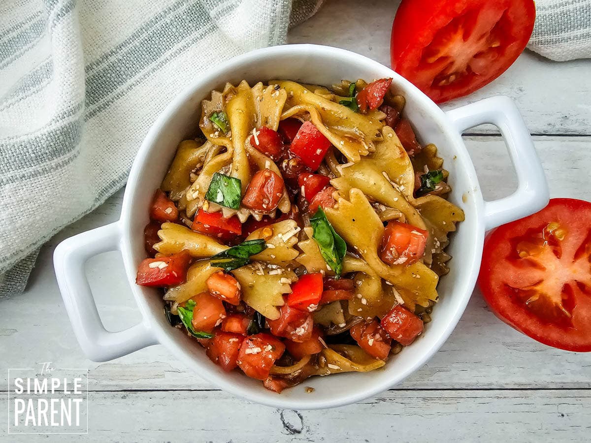 bruschetta pasta salad in white serving bowl with tomatoes