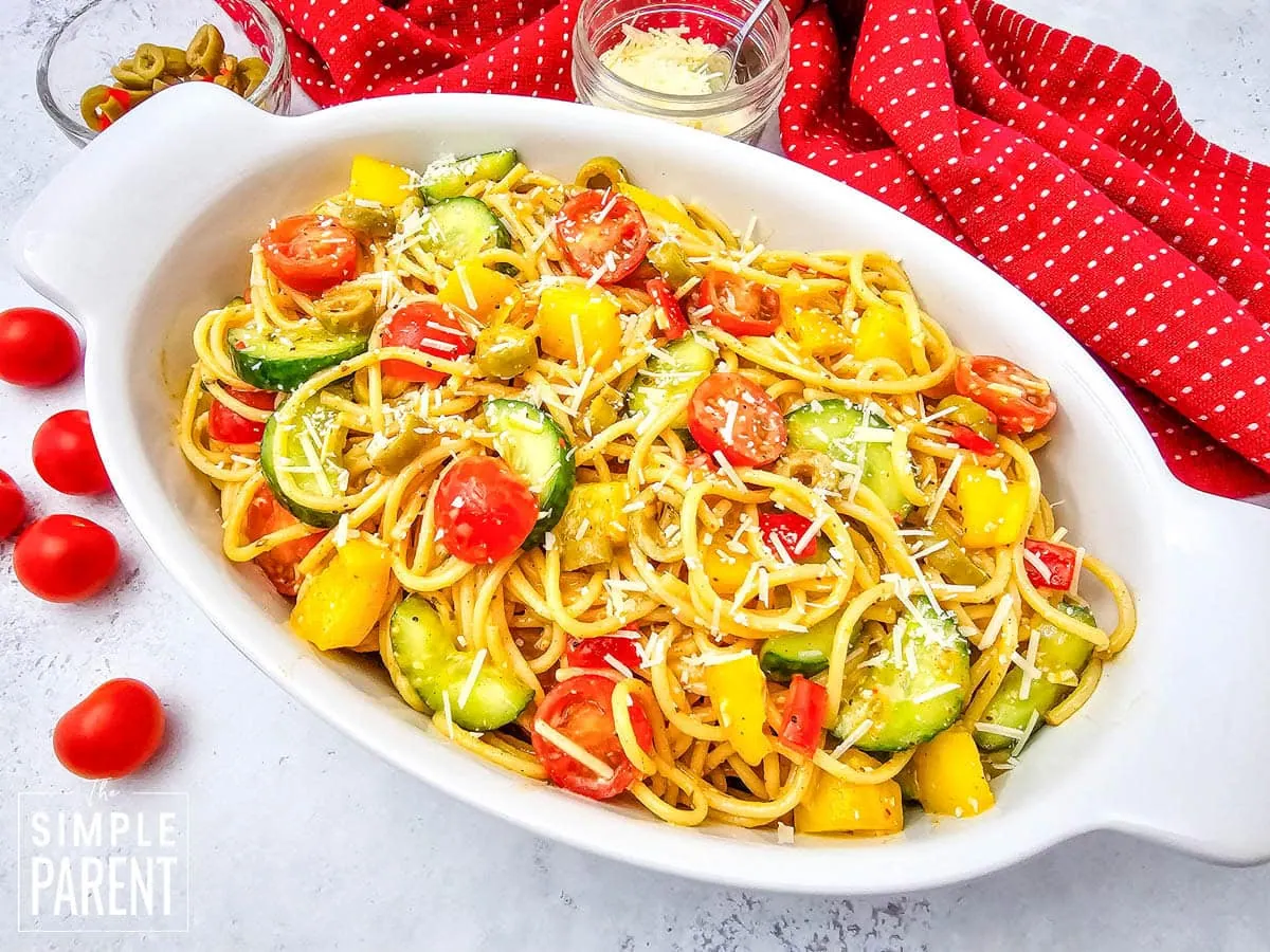 Cold spaghetti salad with tomatoes in white serving dish