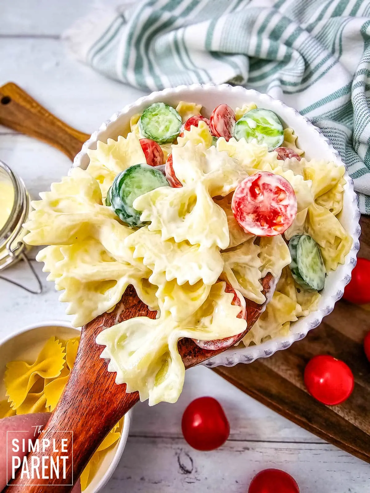 Creamy bowtie salad in white bowl with wooden spoon