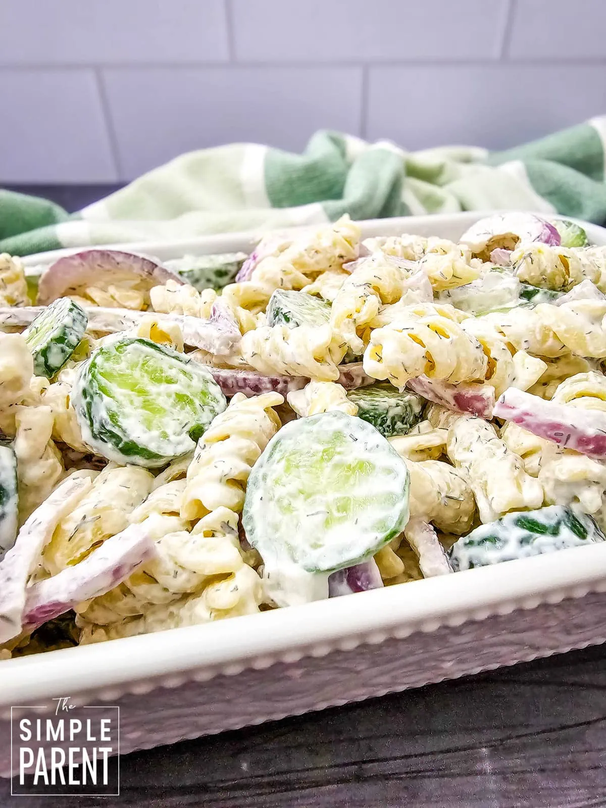 potluck pasta salad with cucumbers and onions in white serving dish