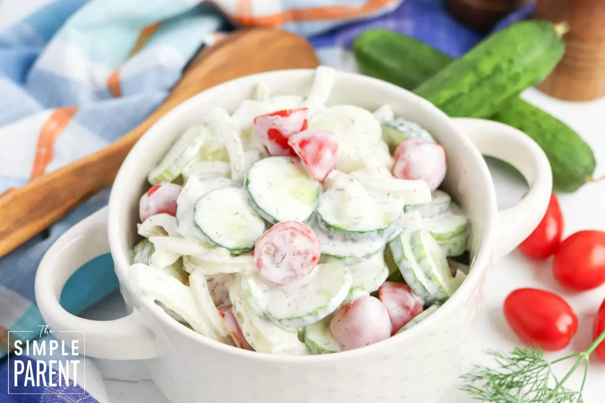cucumber tomato onion salad in white bowl with wooden serving spoon