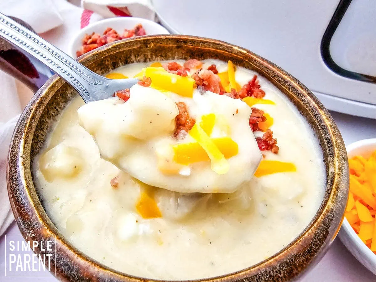 Spoonful of Crockpot Loaded Baked Potato soup of brown soup bowl