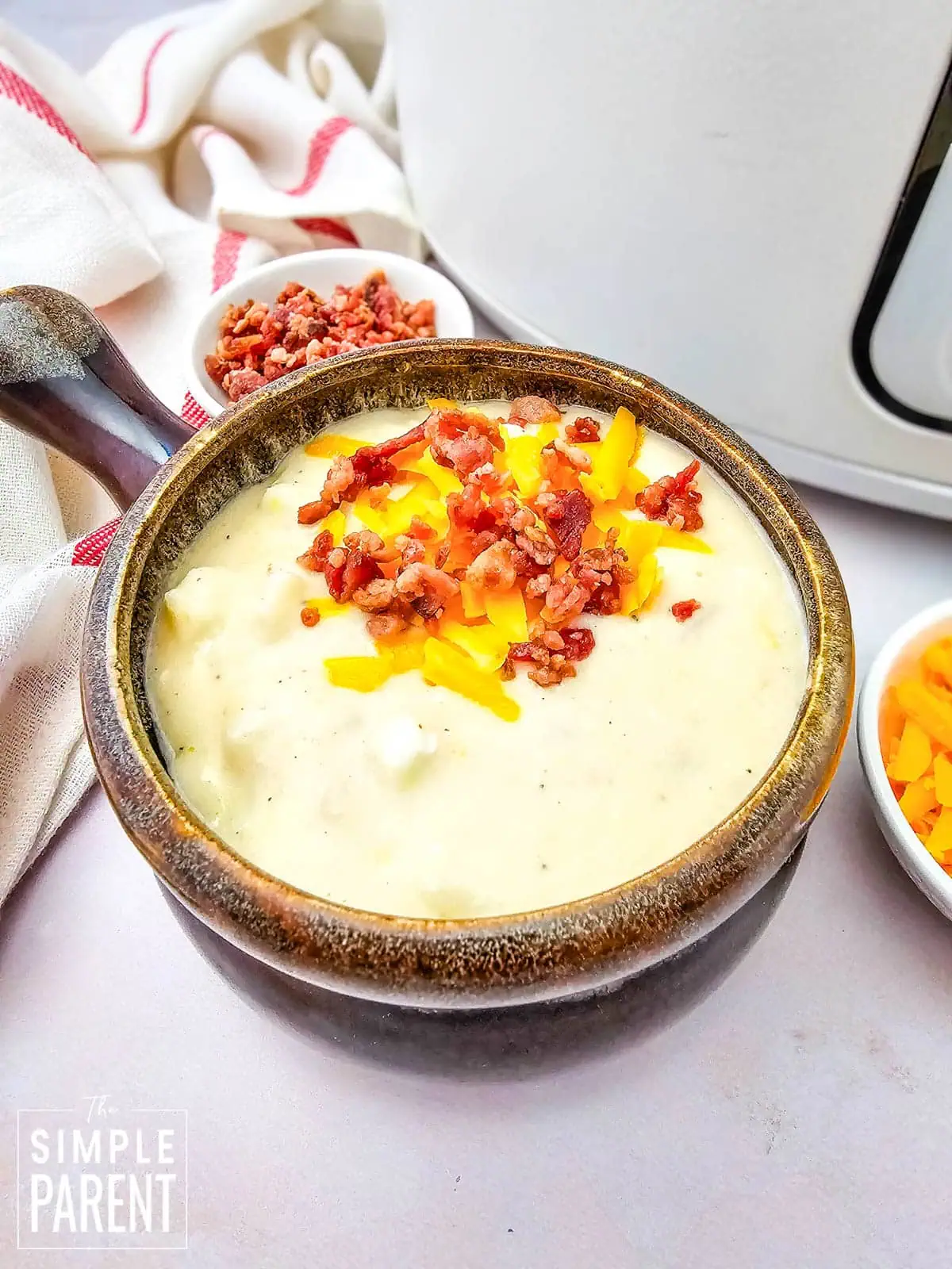 Slow Cooker Loaded Baked Potato soup topped with bacon and cheese in brown ceramic soup bowl